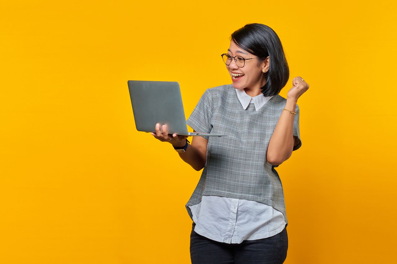 Ecstatic Asian woman with short hair celebrates success using a laptop.