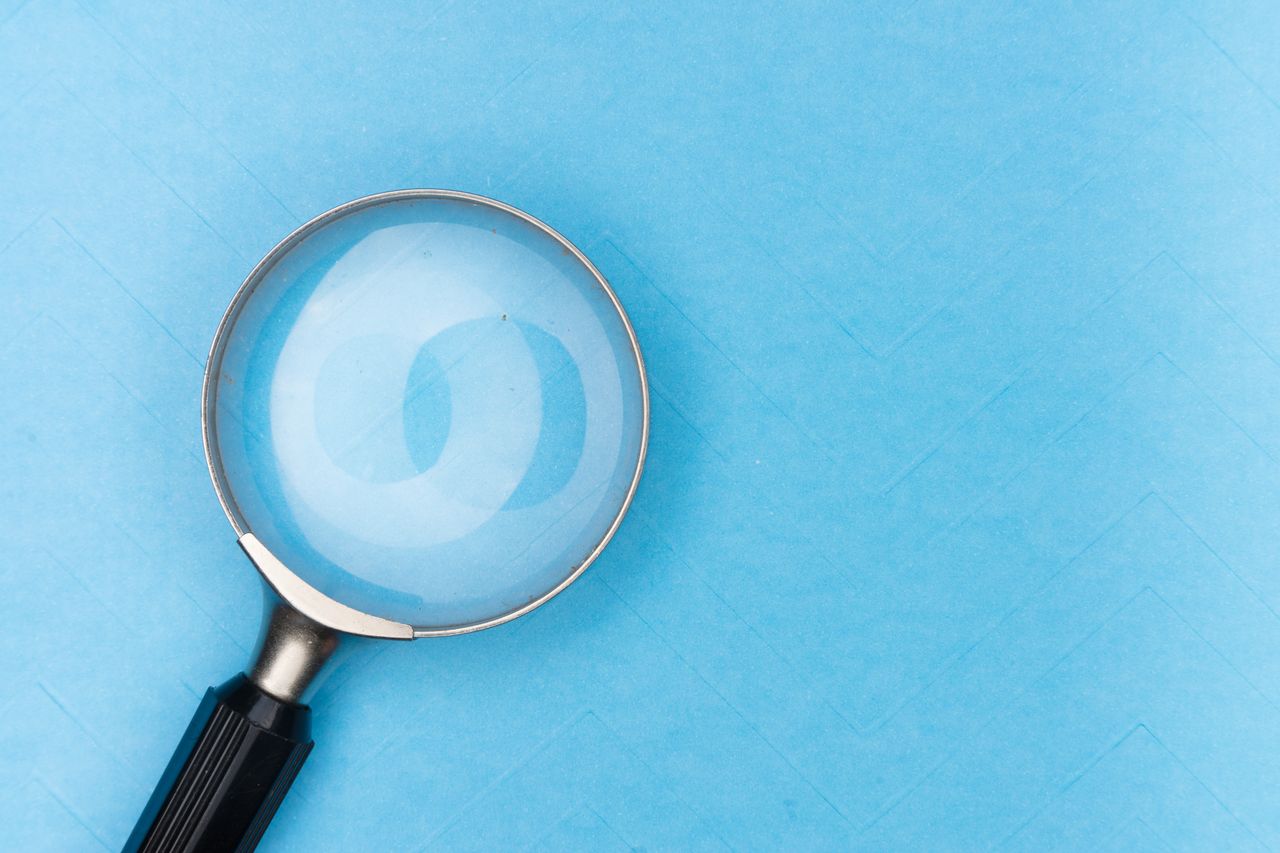 Close-up of a magnifying glass on a blue surface, ideal for search and exploration themes.